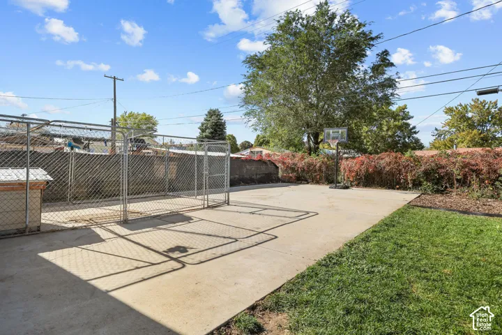 Concrete patio area featuring a chain-link enclosure, integrated basketball hoop, and established perimeter hedging