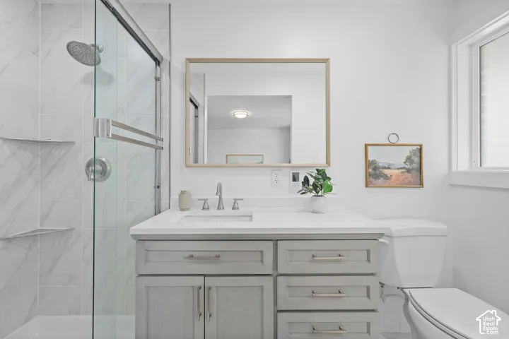 Bathroom featuring a gray shaker-style vanity with a solid-surface countertop, an undermount sink, a glass-enclosed shower with tiled walls and a rainfall showerhead, and a rectangular mirror with a wood frame