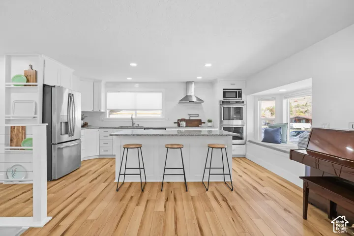Kitchen featuring wood-finish flooring, a central island with stone-finish countertops, stainless steel appliances, built-in wall ovens, and a window-side built-in bench