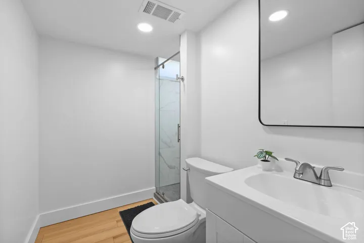 Bathroom featuring wood-finish flooring, a white vanity with an integrated sink, a glass-enclosed shower with tiled walls, and a rectangular mirror with a black frame