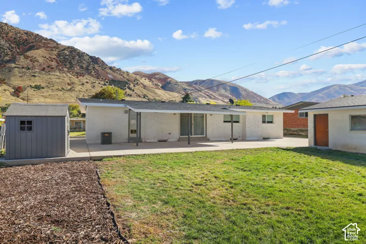 Single-story exterior featuring a white painted brick facade, concrete patio, asphalt shingle roofing, and mountain backdrop