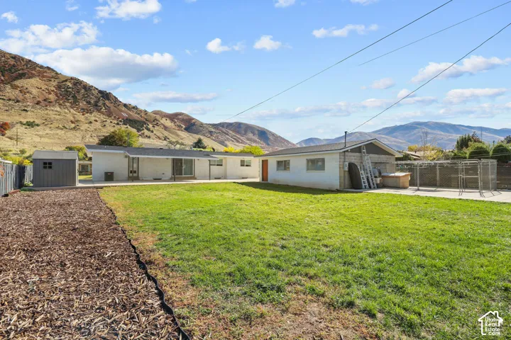 Expansive backyard featuring a large grass lawn, detached garage, storage shed, concrete patio, and mountain backdrop