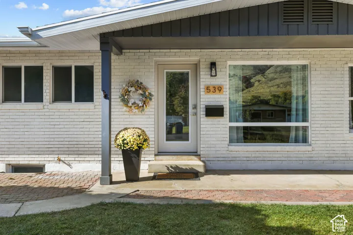 White-painted brick exterior featuring a covered porch, large picture window, stone-paver walkway, and a modern glass-panel entry door