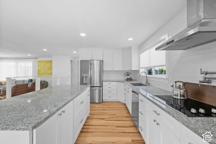 Kitchen featuring white cabinetry, stone countertops, stainless steel appliances, a pot filler faucet, and wood-finish flooring