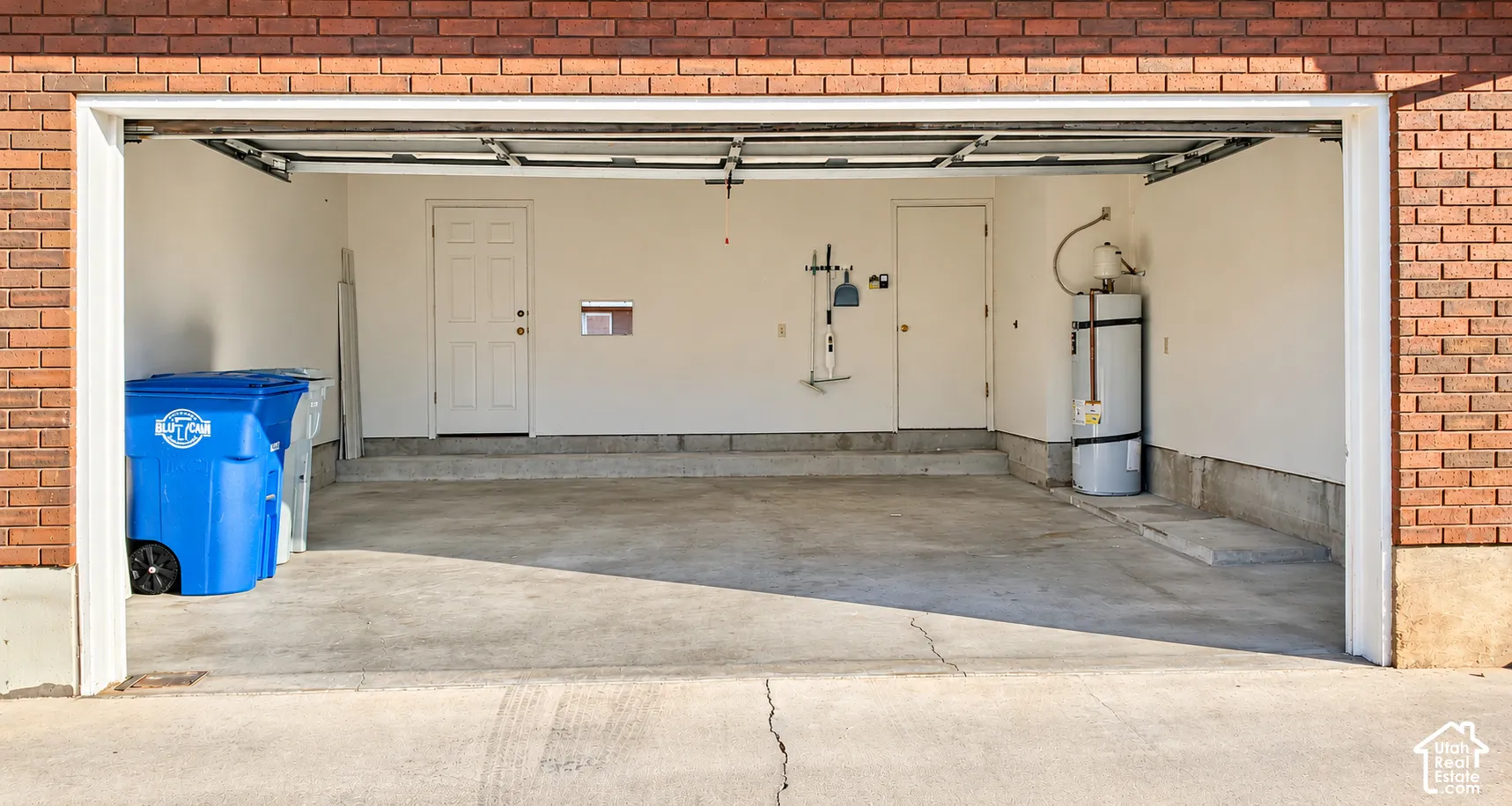 Garage interior featuring brick masonry exterior walls, concrete flooring, dual entry doors, and an integrated water heater