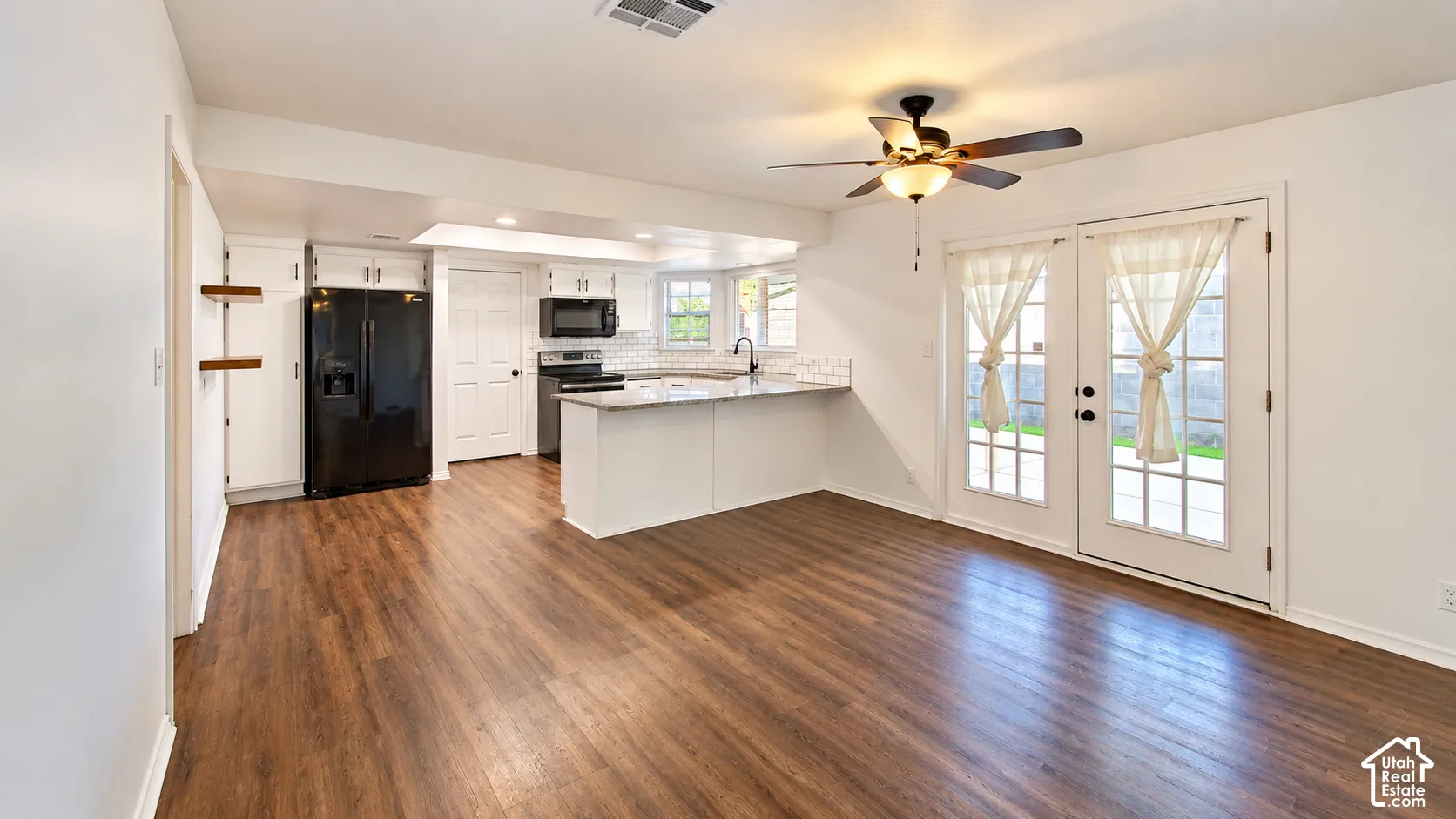 Kitchen featuring stone countertops, white cabinetry, integrated black appliances, wood-finish flooring, and dual French doors