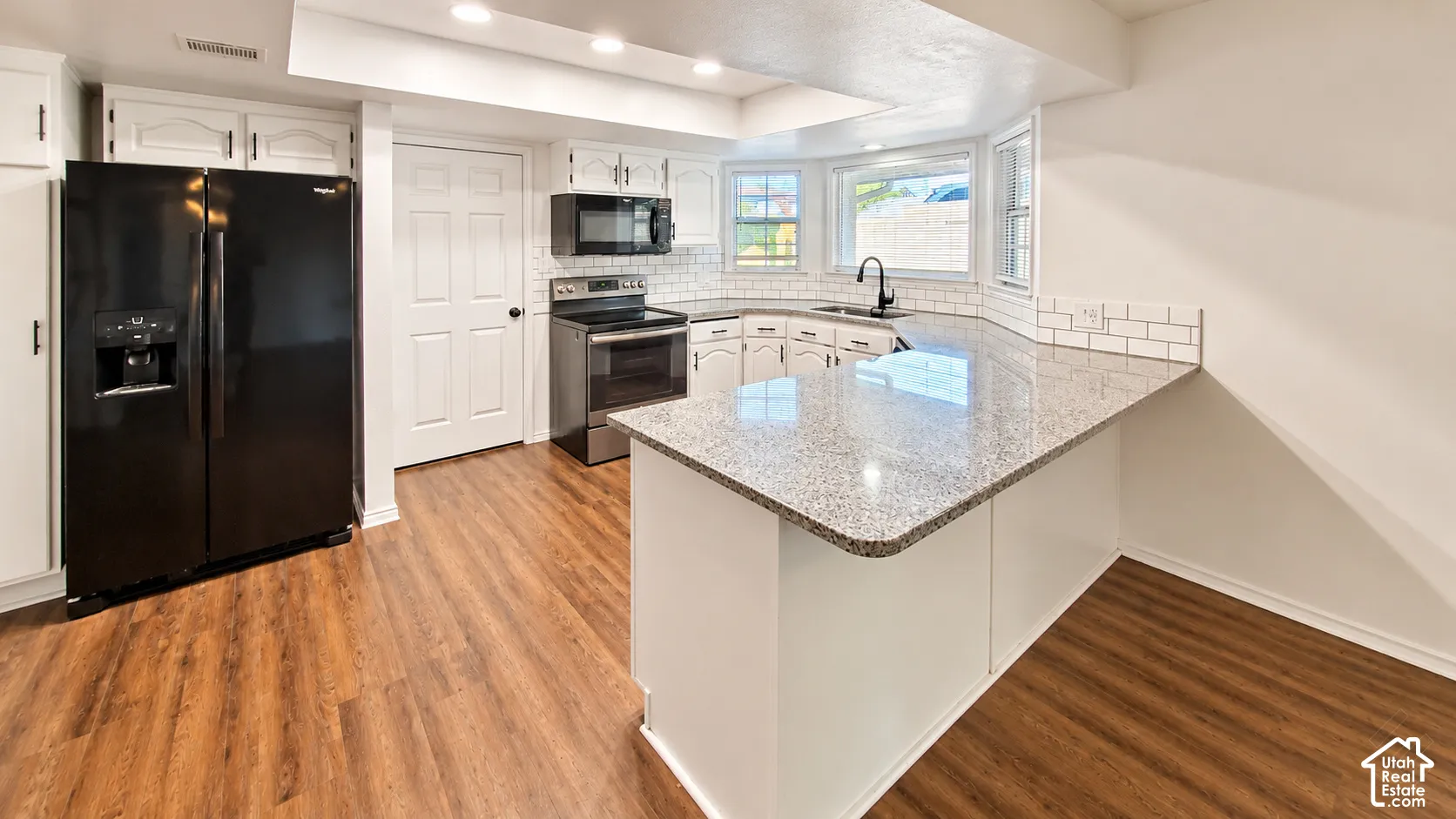 Kitchen featuring stone-finish countertops, subway tile backsplash, white cabinetry, wood-finish flooring, and recessed ceiling lighting