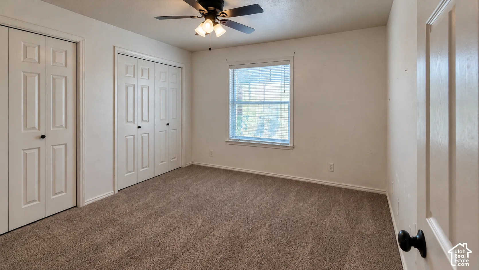 Neutral-toned carpeting, dual bi-fold closets, overhead ceiling fan with light fixture, and horizontal window blinds