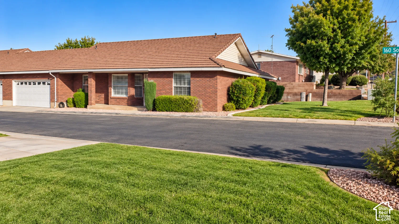 Red brick exterior featuring a multi-gabled tile roof, an attached garage with a sectional door, and landscaped front lawn with manicured shrubbery