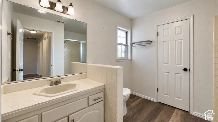 Bathroom featuring a vanity with tile countertop, integrated sink, large wall mirror, multi-bulb lighting, and wood-finish flooring