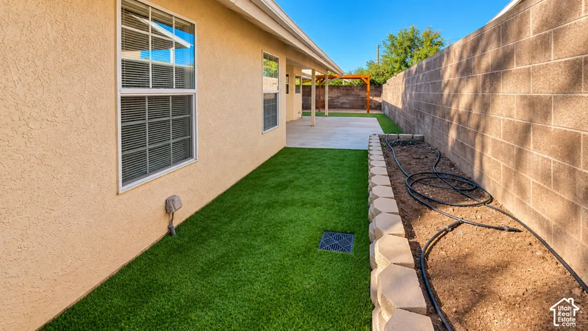Side yard featuring artificial turf, a masonry block perimeter wall, and a raised concrete block planter bed