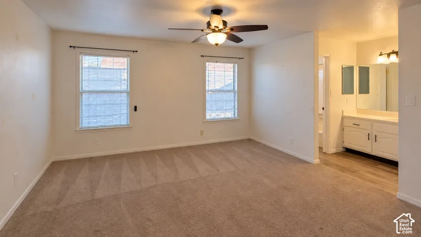 Neutral carpeting, ceiling fan with integrated lighting, dual-pane windows, and a built-in vanity featuring a mirror and wall-mounted lighting