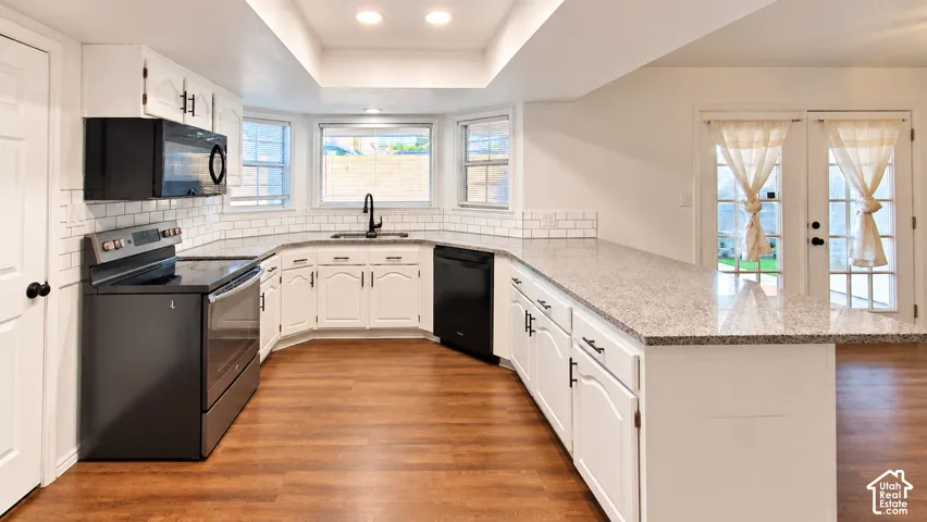 Kitchen featuring white shaker-style cabinetry, speckled stone countertops, subway tile backsplash, wood-finish flooring, and black appliances