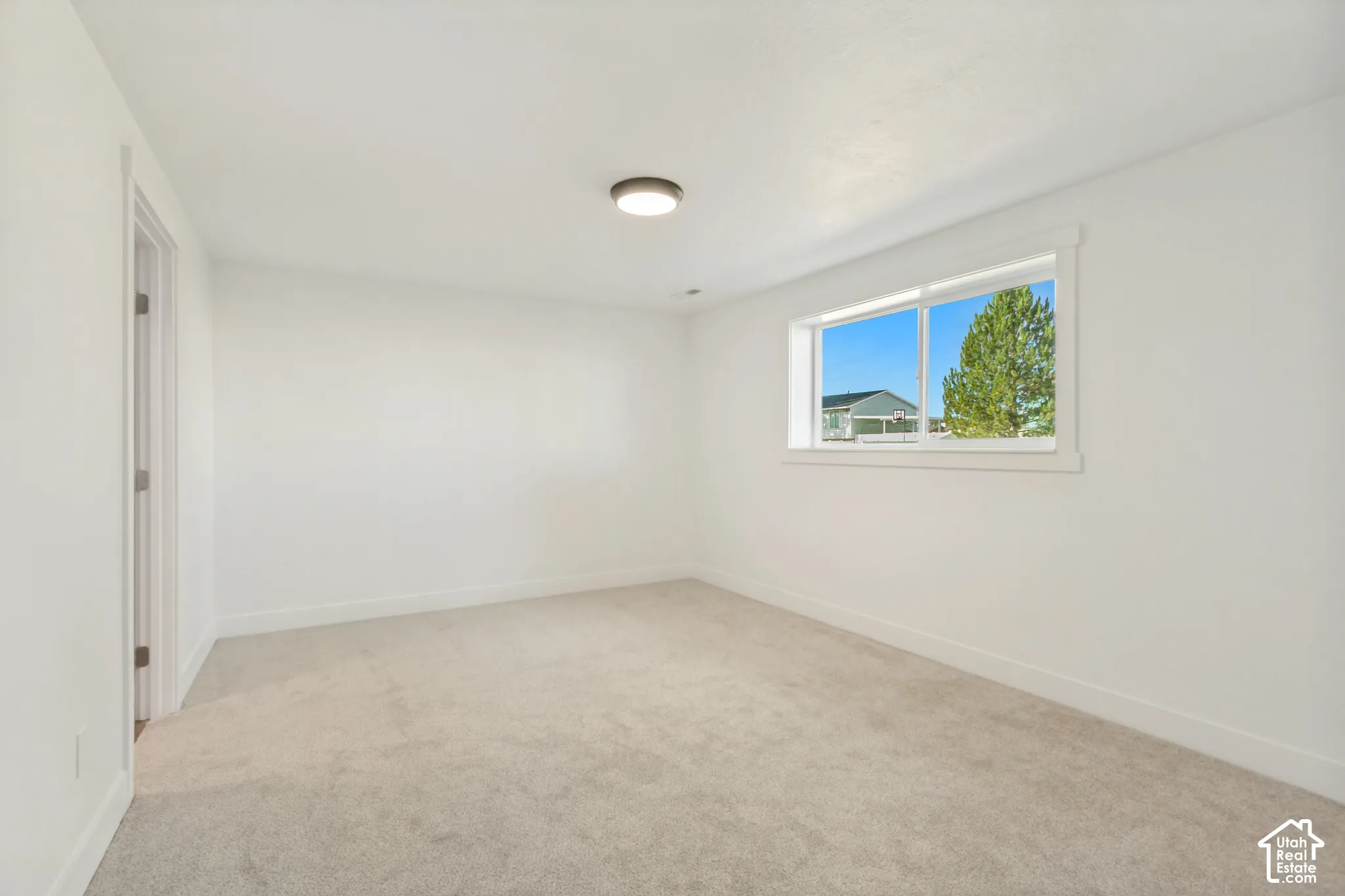 Neutral-toned wall-to-wall carpeting, crisp white walls, sliding window, and flush-mount ceiling lighting
