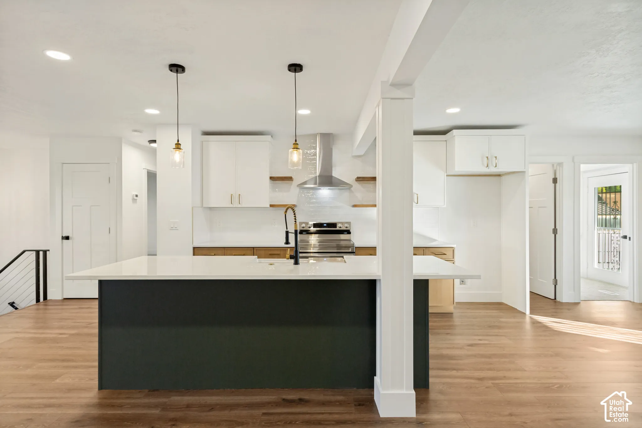 Kitchen featuring a center island with a stone-finish countertop, stainless steel range hood, wood-finish flooring, two glass pendant lights, and two-tone cabinetry