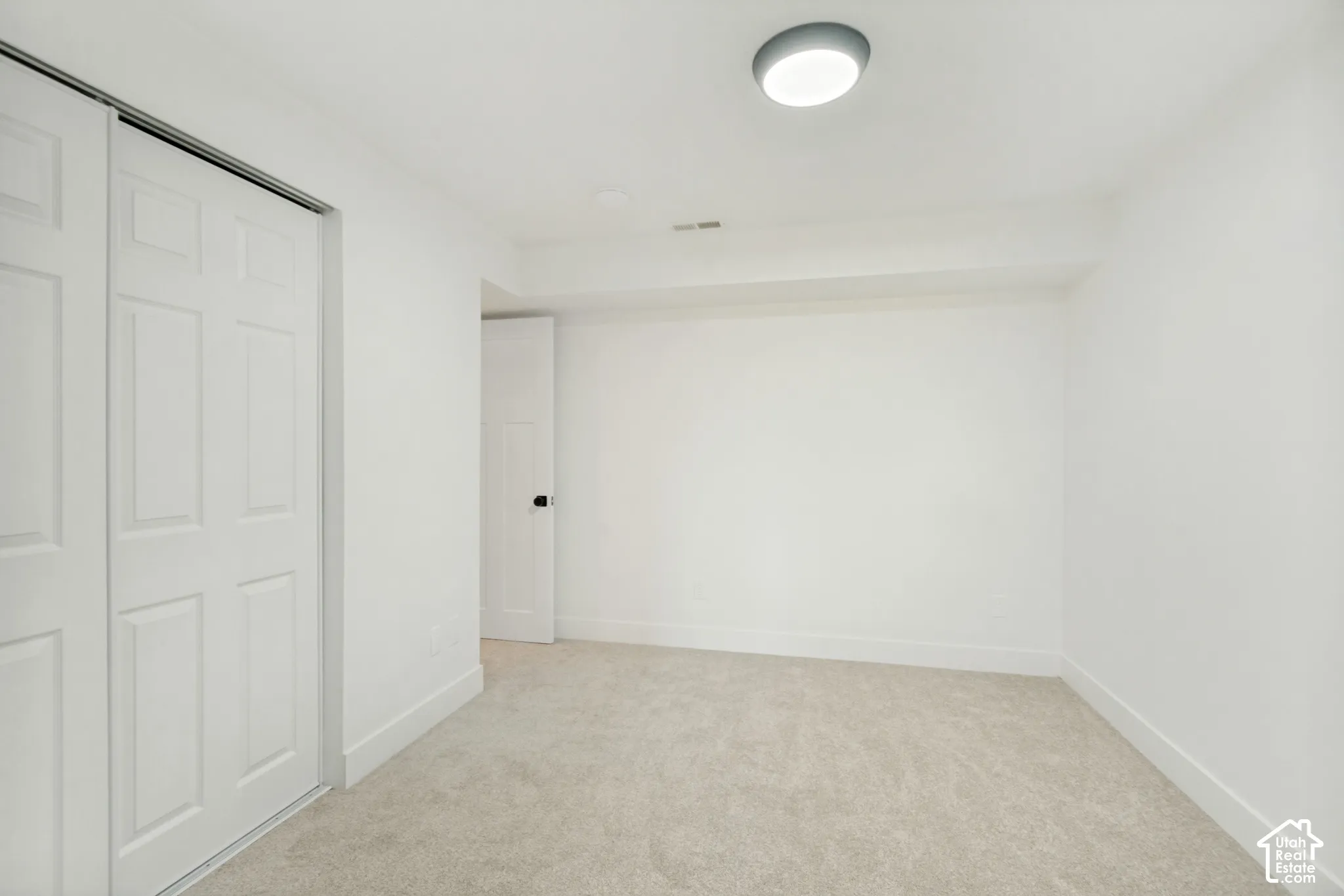 Neutral-toned carpeting, white interior walls, sliding panel closet doors, and flush-mount circular ceiling lighting