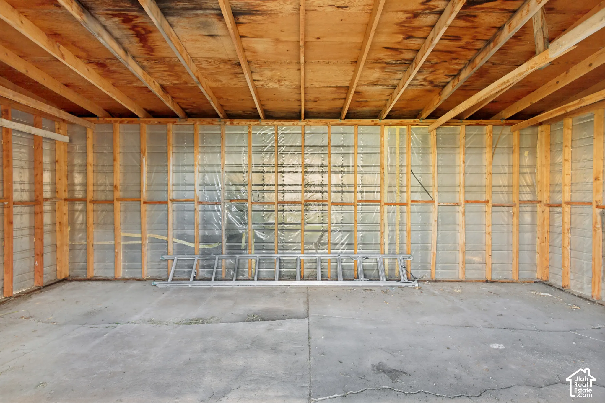 Interior workspace featuring exposed wood-stud framing, unfinished rafter ceiling, reflective vapor barrier insulation, and concrete slab flooring