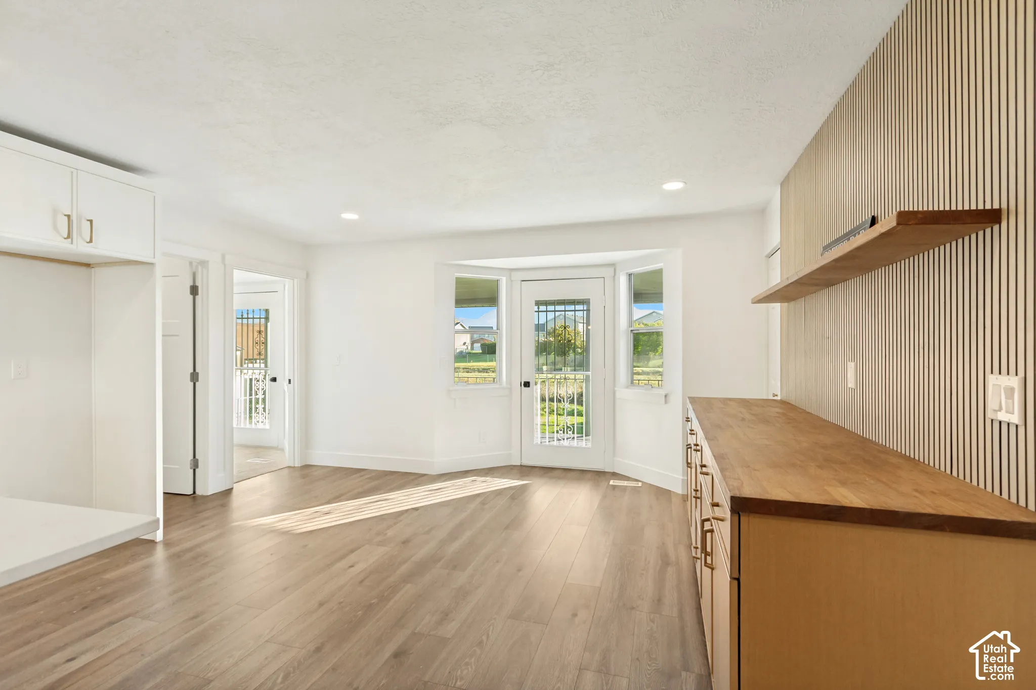 Room featuring wood-finish flooring, a wood-slat accent wall, built-in cabinetry with a wood countertop, and a bay window configuration with a glass-paneled door