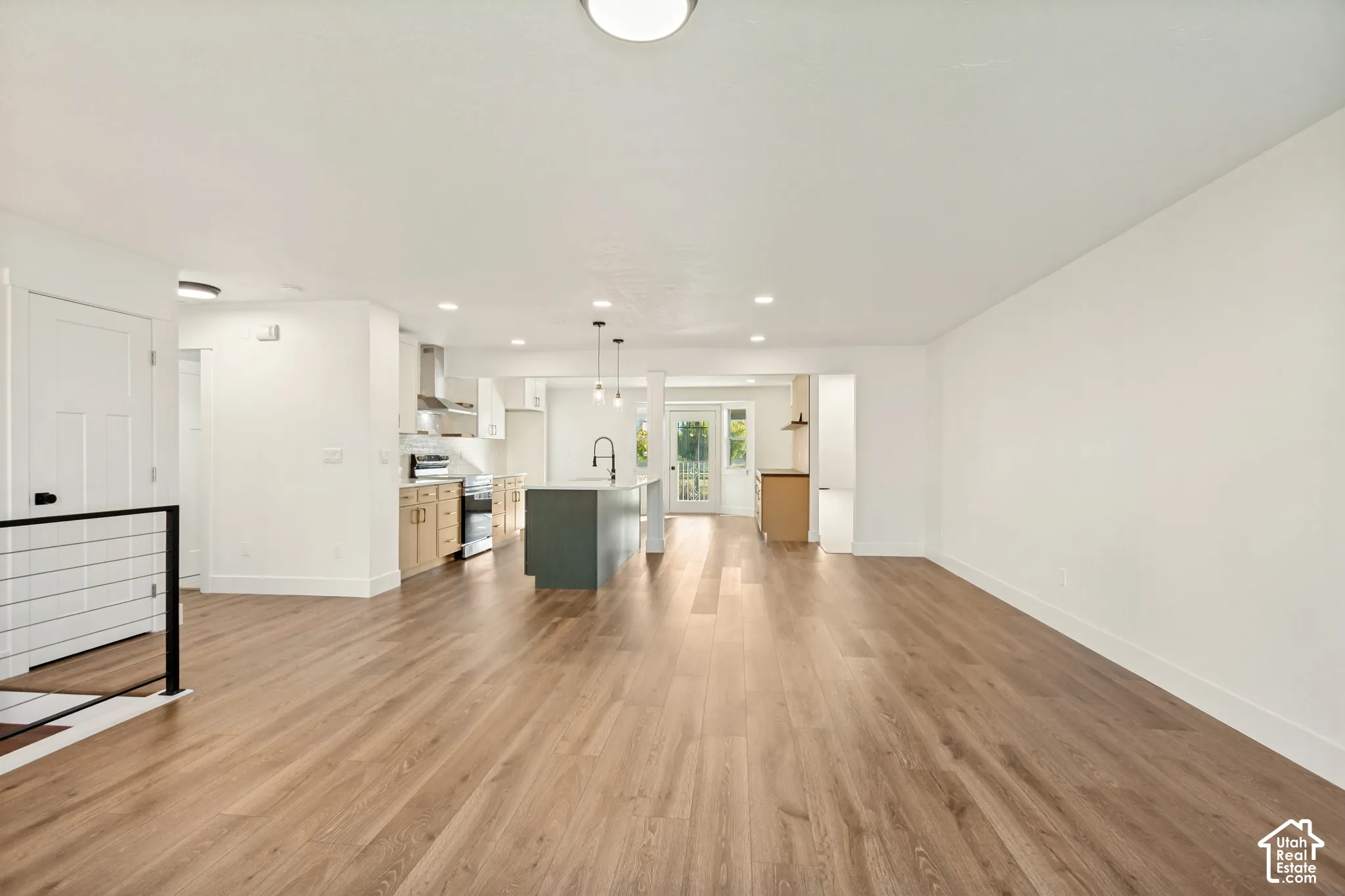 Open-concept area featuring wood-finish flooring, a central kitchen island with a dark-tone base, recessed lighting, and a stainless steel range hood