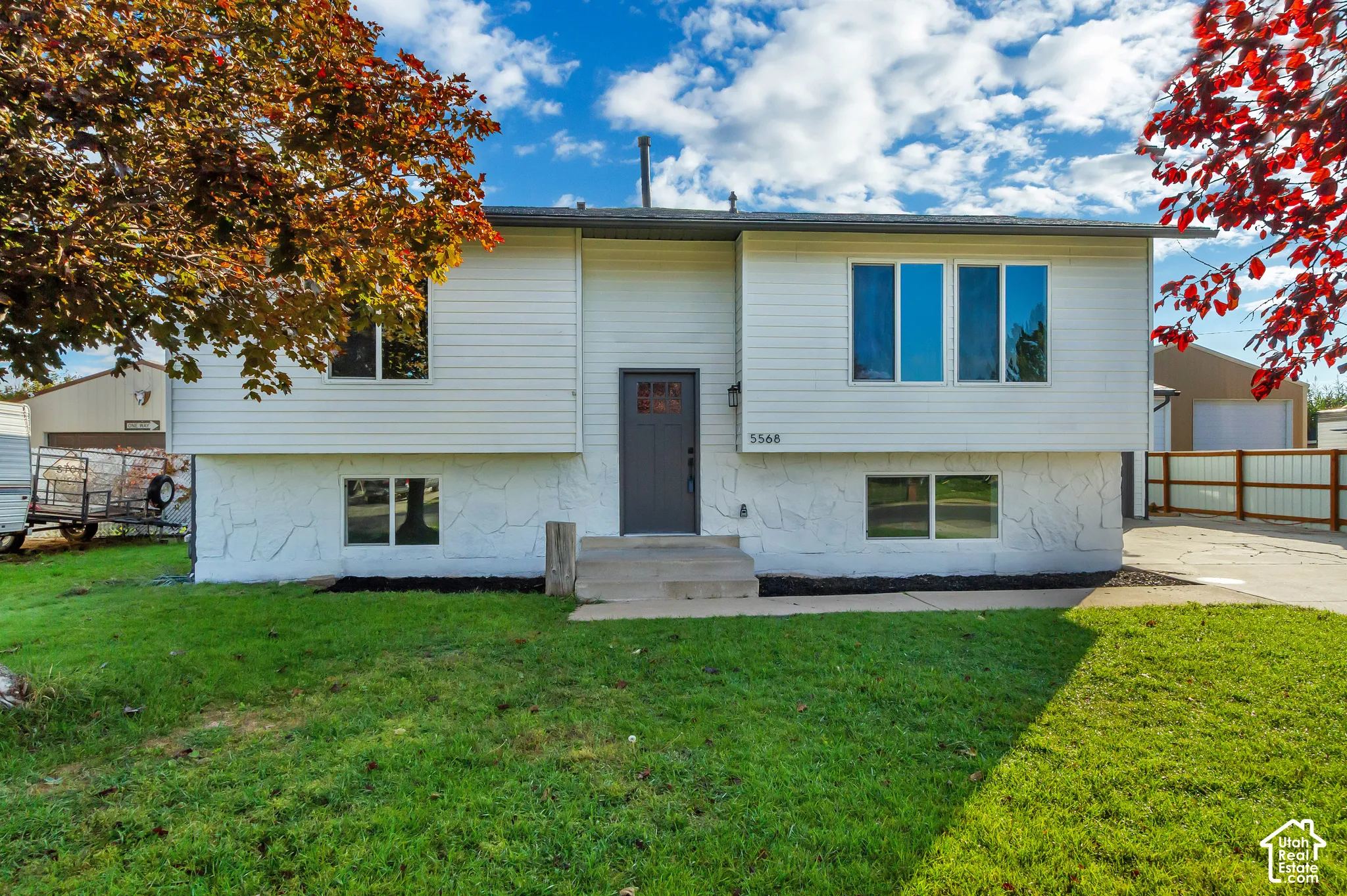 Split-level exterior featuring white horizontal siding, stone-textured lower facade, front door with glass insert, and concrete entry steps
