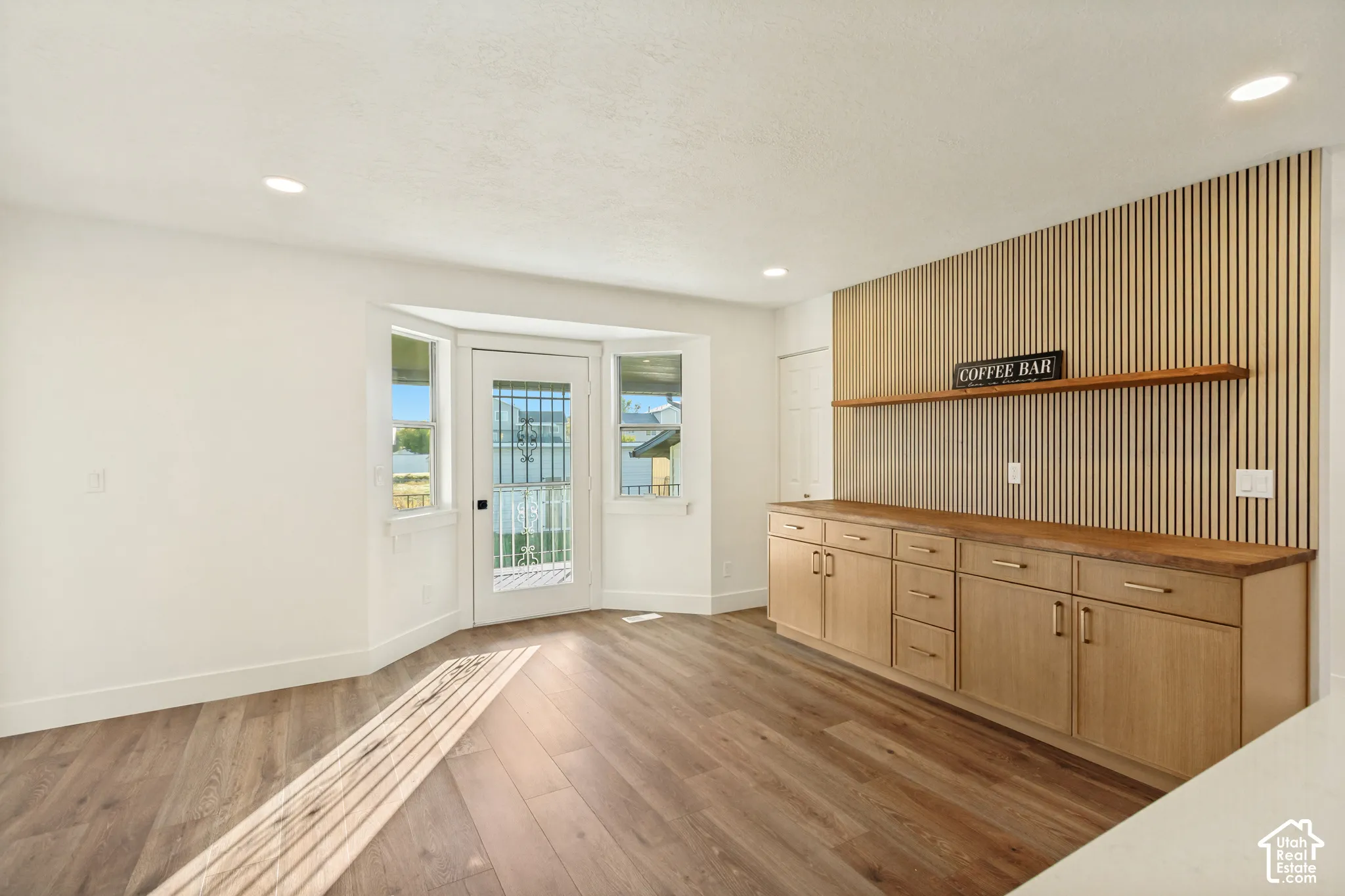 Interior featuring wood-finish flooring, built-in lower cabinetry with drawers, a floating wood-finish wall shelf, a vertically slatted wood-finish accent wall, and an exterior door with flanking windows