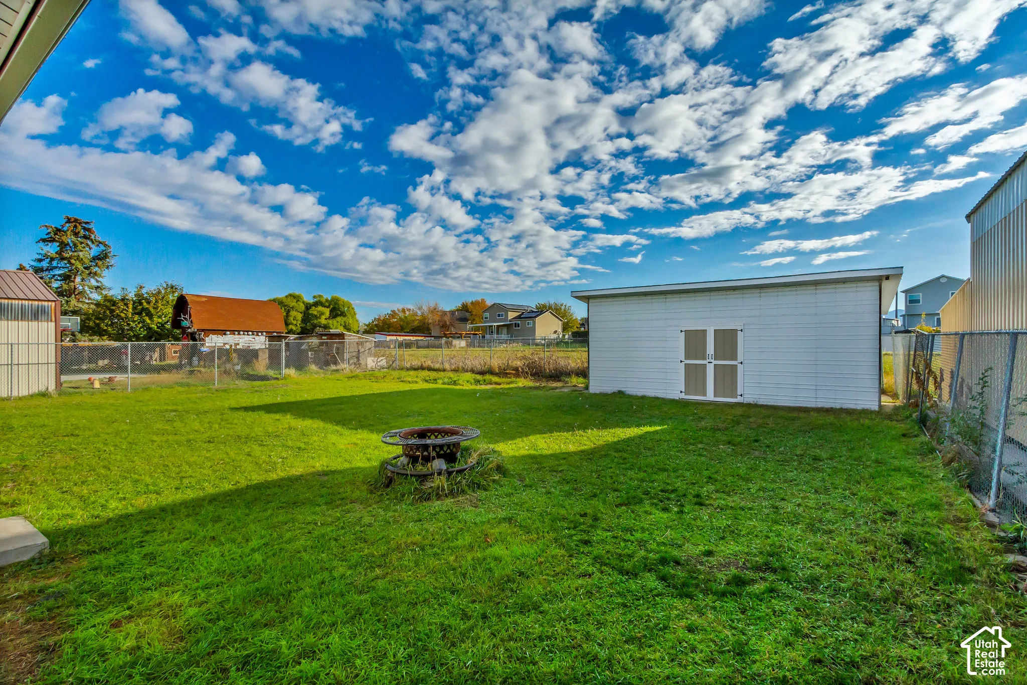 Spacious backyard featuring a manicured lawn, a detached white structure, and a metal chain-link perimeter fence