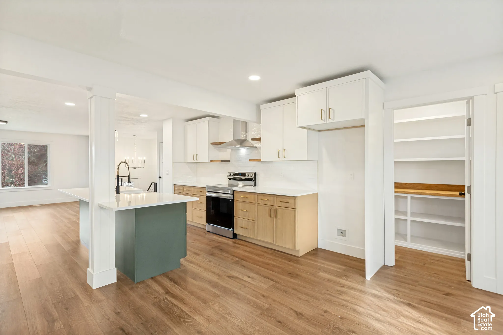 Kitchen featuring wood-finish flooring, two-tone cabinetry with white uppers and natural-finish lowers, quartz countertops, a stainless steel range hood, and a walk-in pantry with built-in shelving
