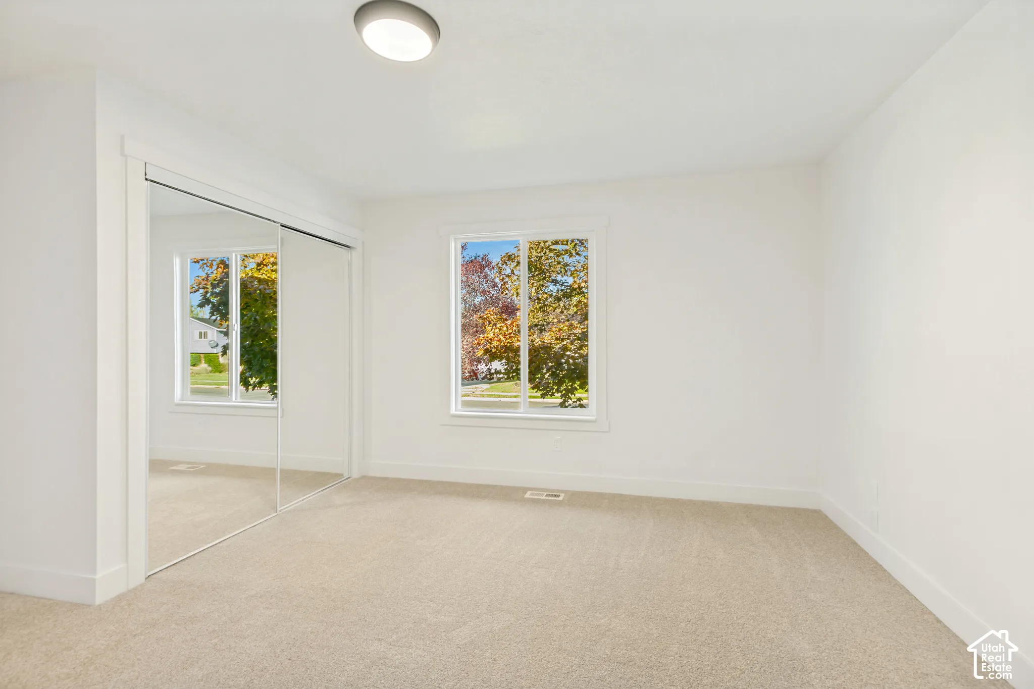 Interior space featuring neutral-toned carpeting, mirrored sliding closet doors, a single window with white trim, and a flush-mount overhead light fixture