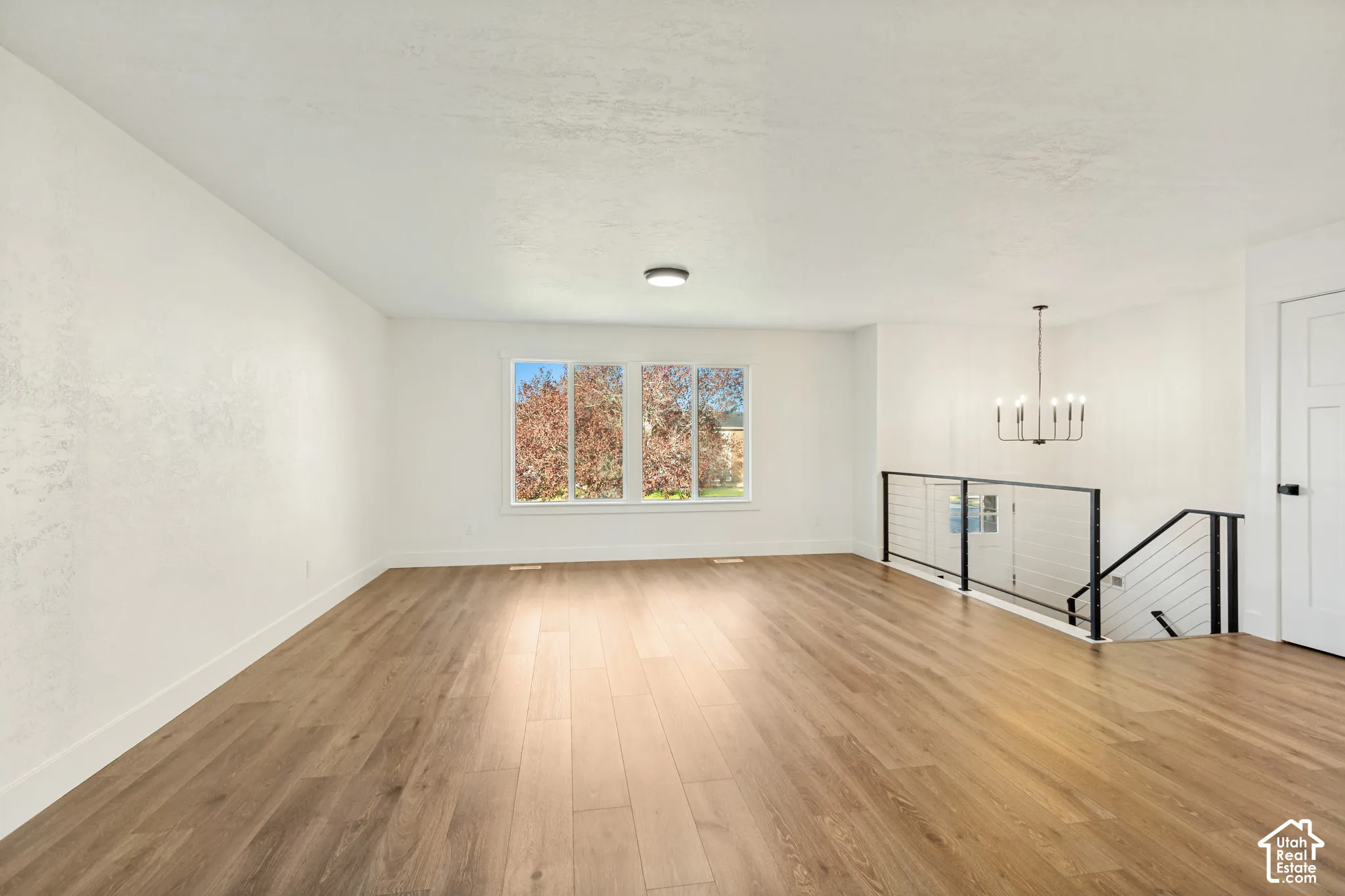 Open floor plan featuring wood-finish flooring, metal cable railing, a multi-arm chandelier, and neutral walls