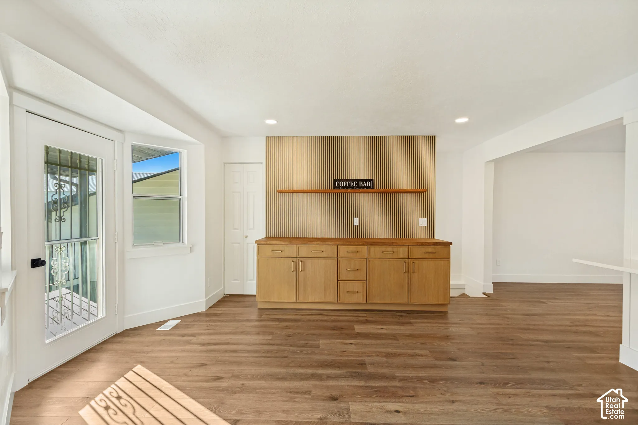 Wood-finish flooring, custom built-in cabinetry, vertical slat wall accent, floating wooden shelf, and full-light glass door