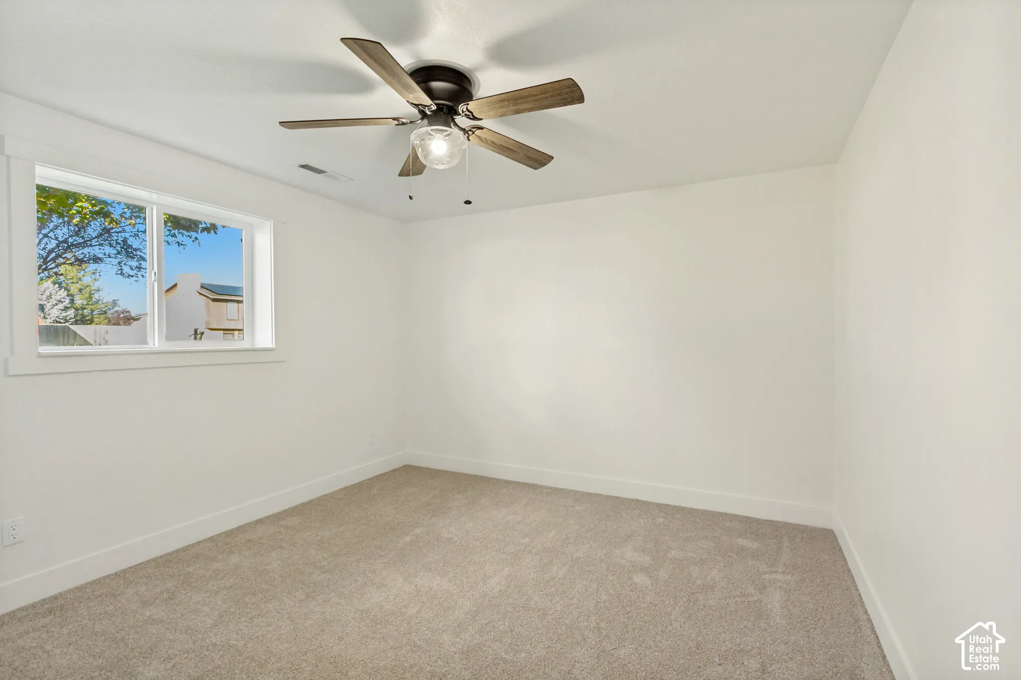 Neutral interior featuring light-toned wall-to-wall carpeting, a multi-blade ceiling fan with integrated light fixture, and a sliding window with wide white casing