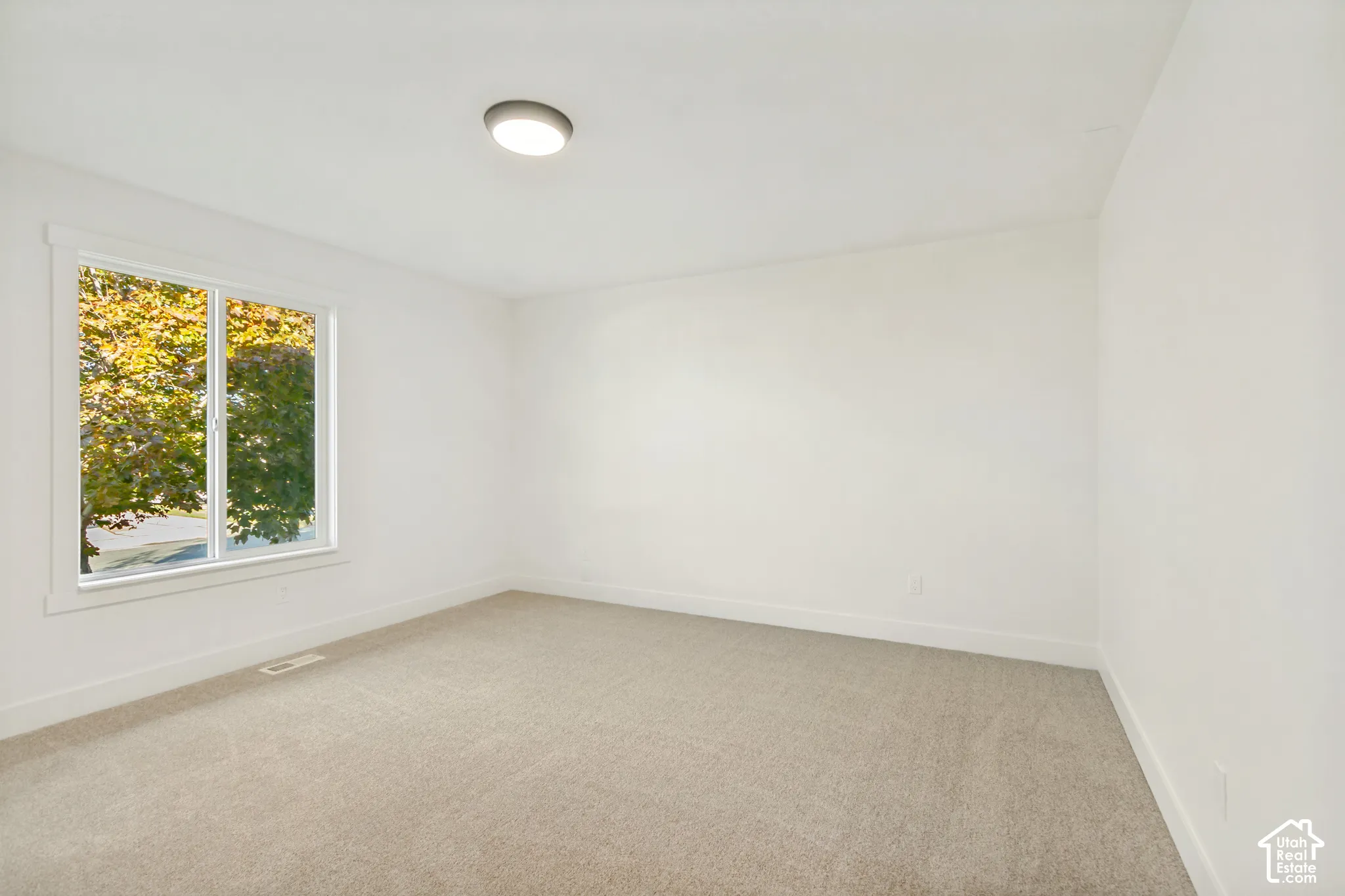 Neutral-toned wall-to-wall carpeting, crisp white walls, and a recessed ceiling light fixture, accented by a single-pane window featuring thick white casing