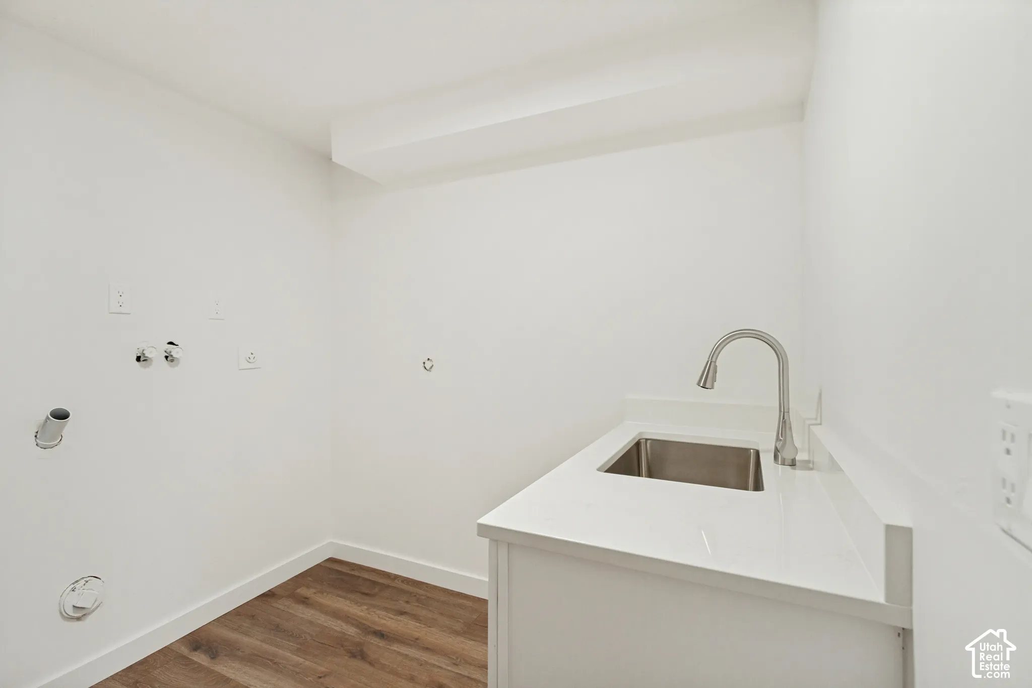 Utility area featuring wood-finish flooring, a white cabinet with a stone-surface countertop, an integrated stainless steel basin, and a high-arch pull-down faucet