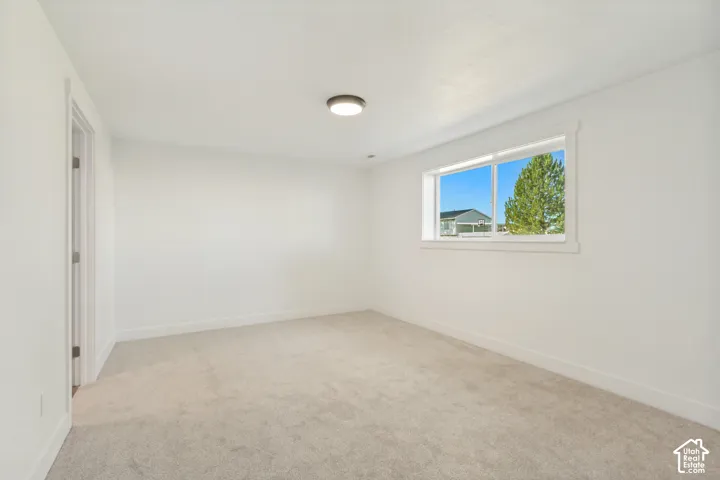 Neutral-toned wall-to-wall carpeting, crisp white walls, sliding window, and flush-mount ceiling lighting