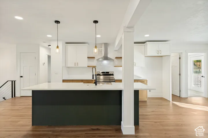 Kitchen featuring a center island with a stone-finish countertop, stainless steel range hood, wood-finish flooring, two glass pendant lights, and two-tone cabinetry