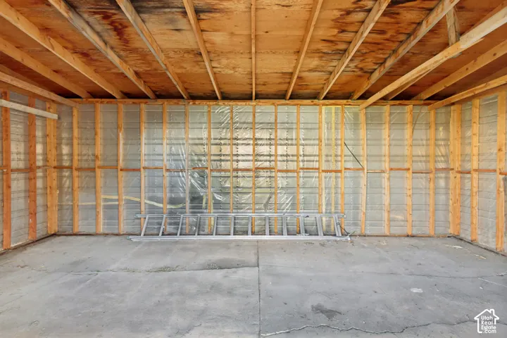 Interior workspace featuring exposed wood-stud framing, unfinished rafter ceiling, reflective vapor barrier insulation, and concrete slab flooring