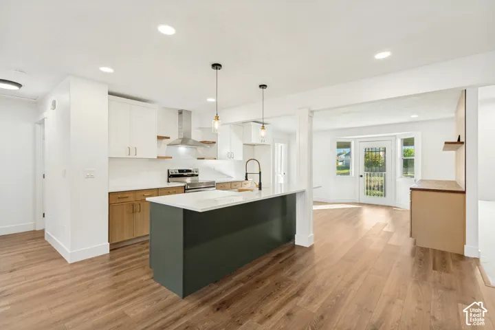 Kitchen featuring white upper cabinetry, lower wood-finish cabinets, a charcoal-colored center island with a stone-style countertop, stainless steel range hood, and wood-finish flooring