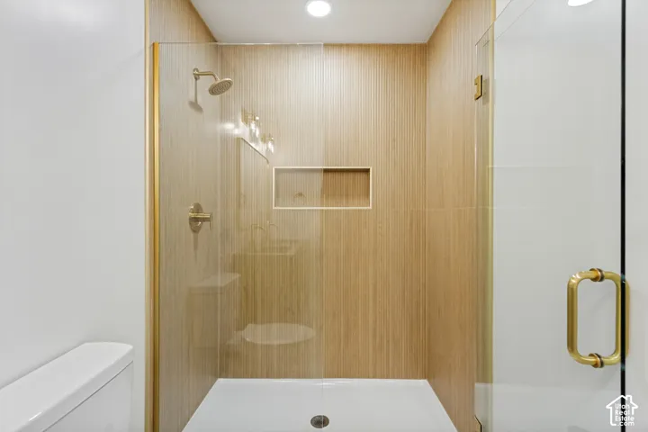 Walk-in shower featuring vertical wood-finish wall tile, a recessed niche, frameless glass door with gold-toned hardware, and a matching gold-toned shower fixture