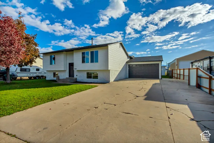 Split-level exterior featuring white horizontal siding, a concrete driveway, an attached garage, and a wood and wire fence
