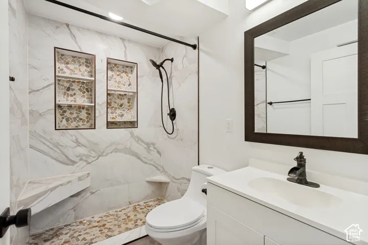 Bathroom featuring a walk-in shower with large-format tile surround, dual built-in recessed wall niches, a pebble-stone floor, and a modern vanity with a wide-set faucet