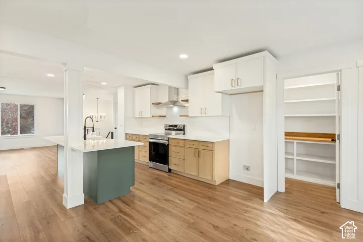 Kitchen featuring wood-finish flooring, two-tone cabinetry with white uppers and natural-finish lowers, quartz countertops, a stainless steel range hood, and a walk-in pantry with built-in shelving