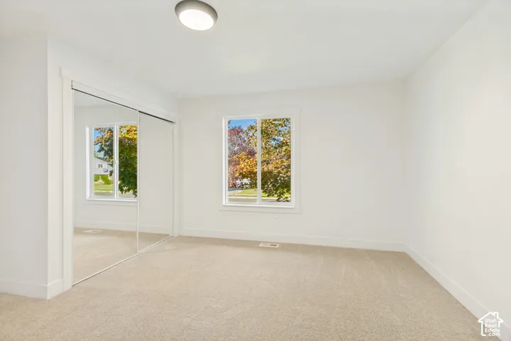 Interior space featuring neutral-toned carpeting, mirrored sliding closet doors, a single window with white trim, and a flush-mount overhead light fixture