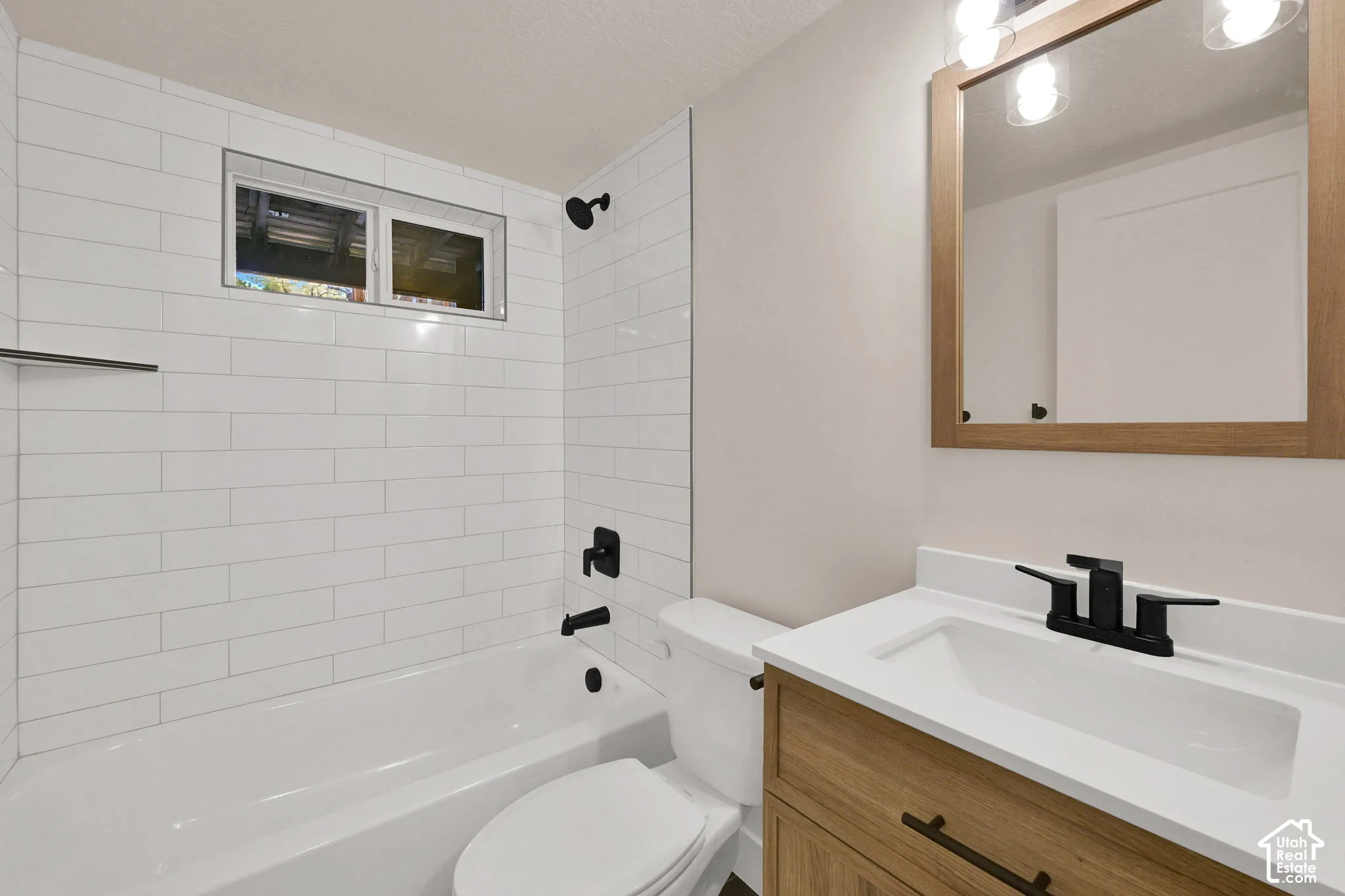 Bathroom featuring white subway tile tub surround, wood-finish vanity with a white countertop, matte black fixtures, and a wood-framed mirror