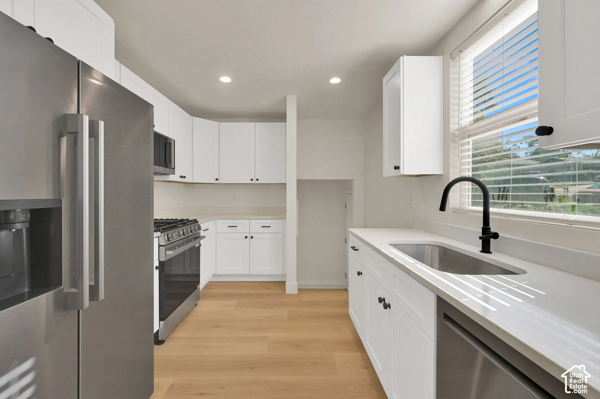Kitchen featuring white shaker-style cabinetry, stainless steel appliances, quartz countertops, wood-finish flooring, and a matte black gooseneck faucet