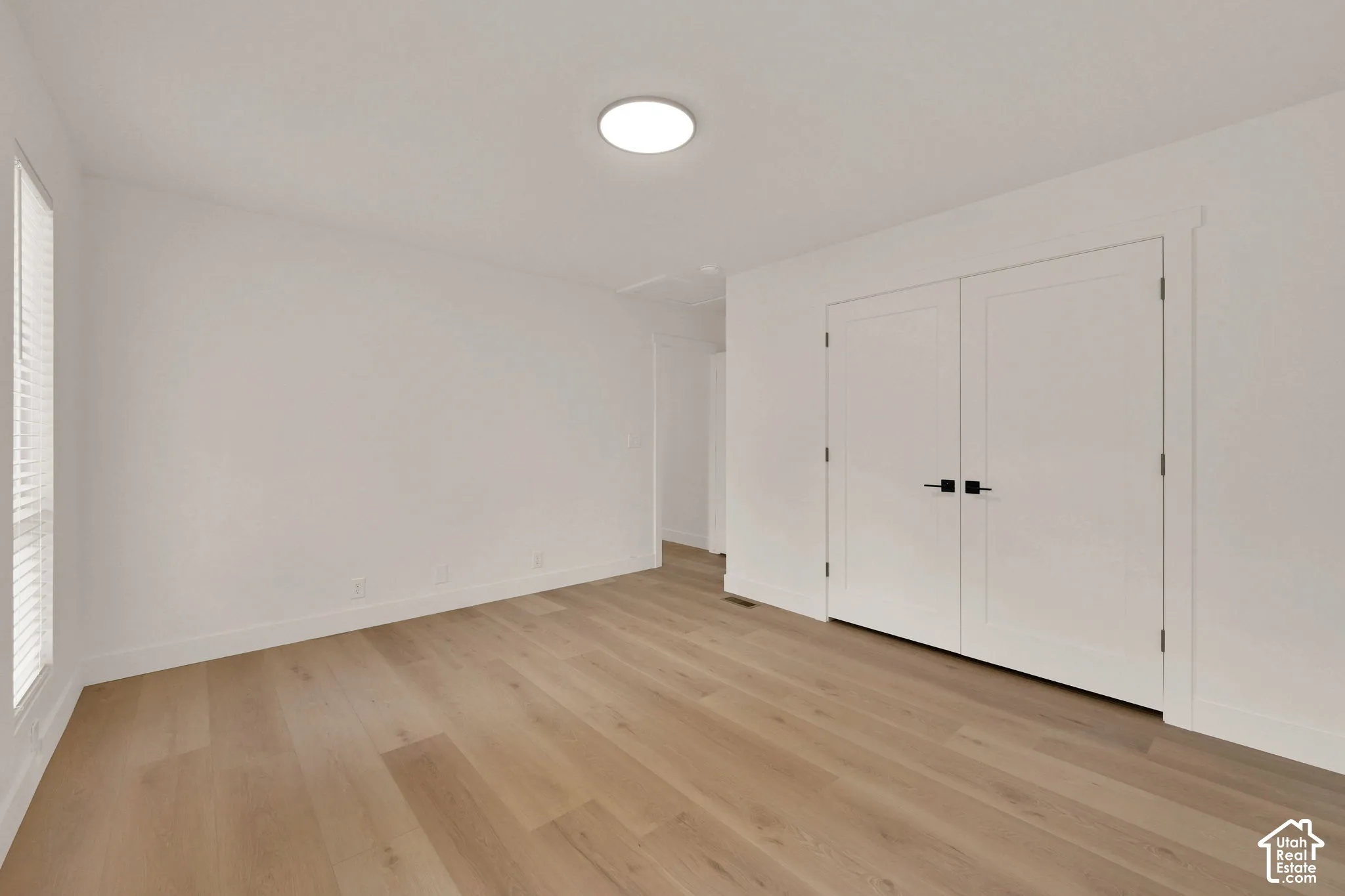 Neutral-toned room featuring wood-finish flooring, double-panel doors with matte black hardware, and a flush-mount ceiling light
