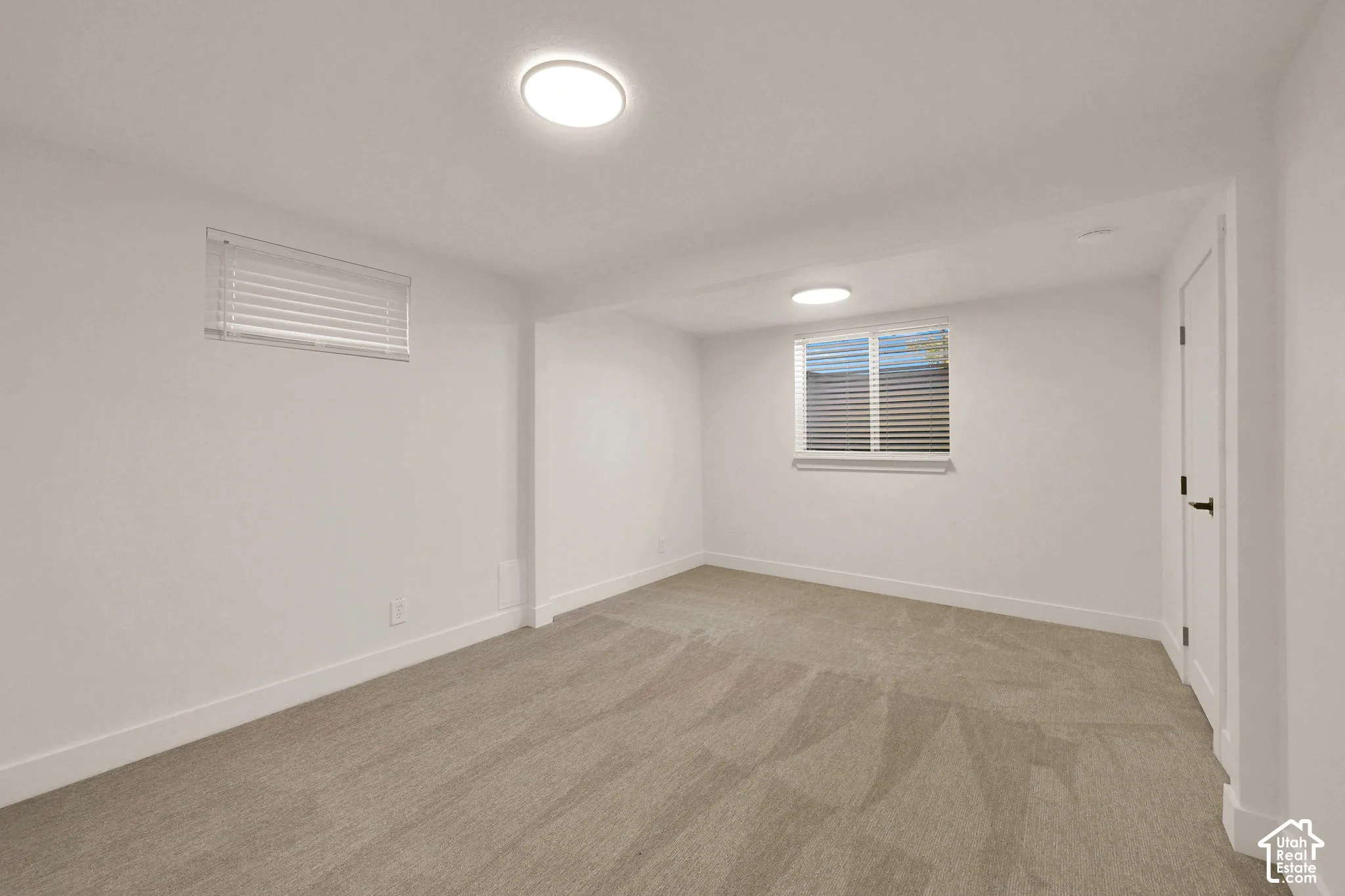 Neutral-toned wall-to-wall carpeting, two dual-flush mount ceiling lights, and dual windows equipped with horizontal slat blinds