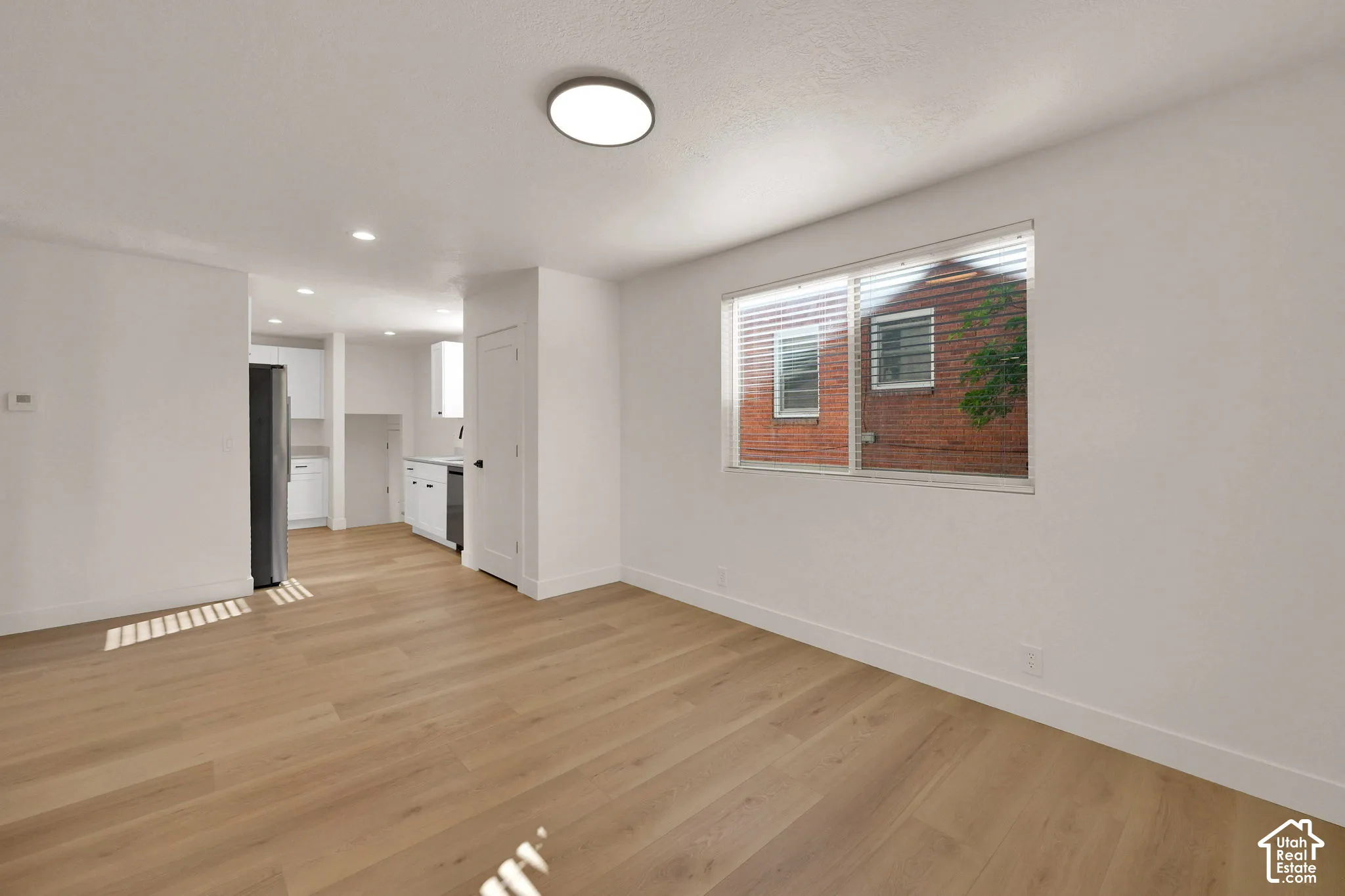 Interior space featuring wood-finish flooring, white walls, flush-mount lighting, and large horizontal window with integrated blinds