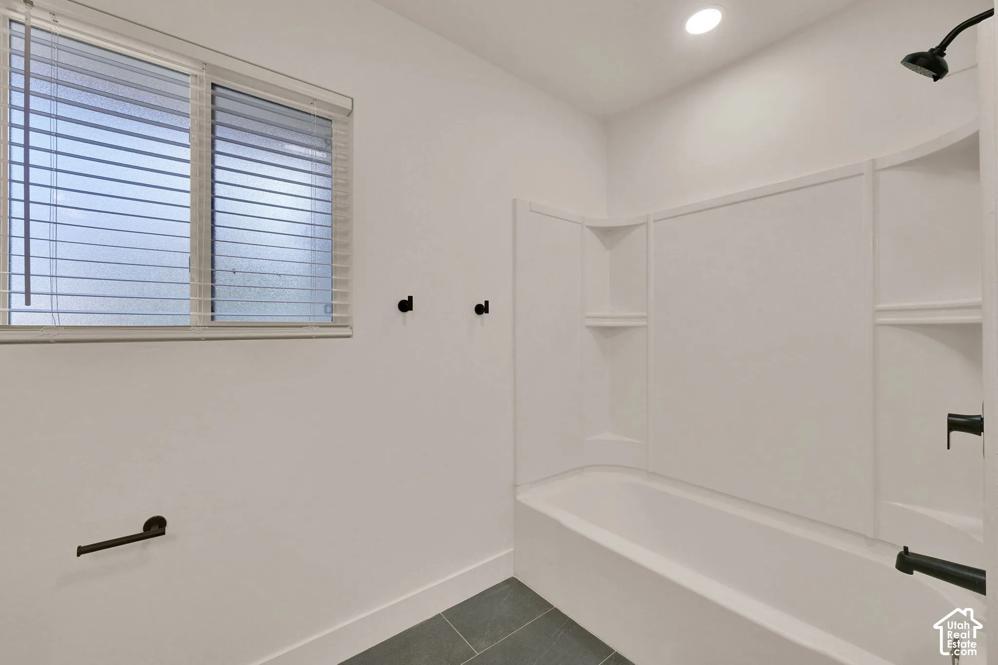 Bathroom featuring a composite tub surround with integrated shelving, matte black plumbing fixtures, recessed ceiling lighting, and large-format tile flooring