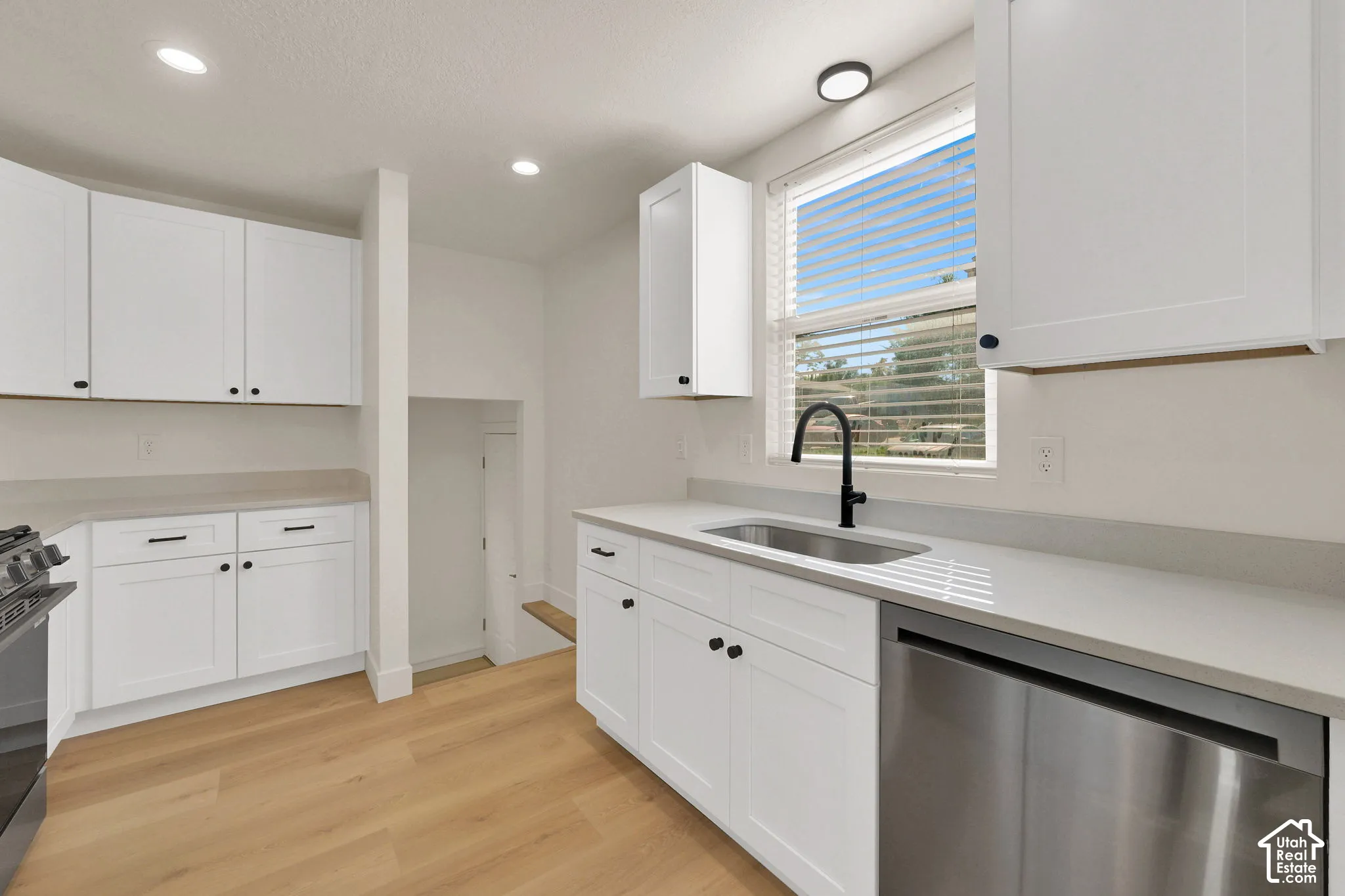 Kitchen featuring white shaker-style cabinetry, neutral countertops, stainless steel appliances, matte black hardware, and wood-finish flooring