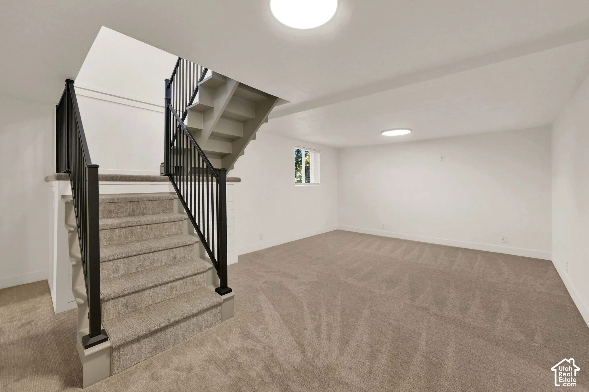 Open interior space featuring neutral carpeting, a staircase with matte black metal railings, and dual flush-mount ceiling lighting